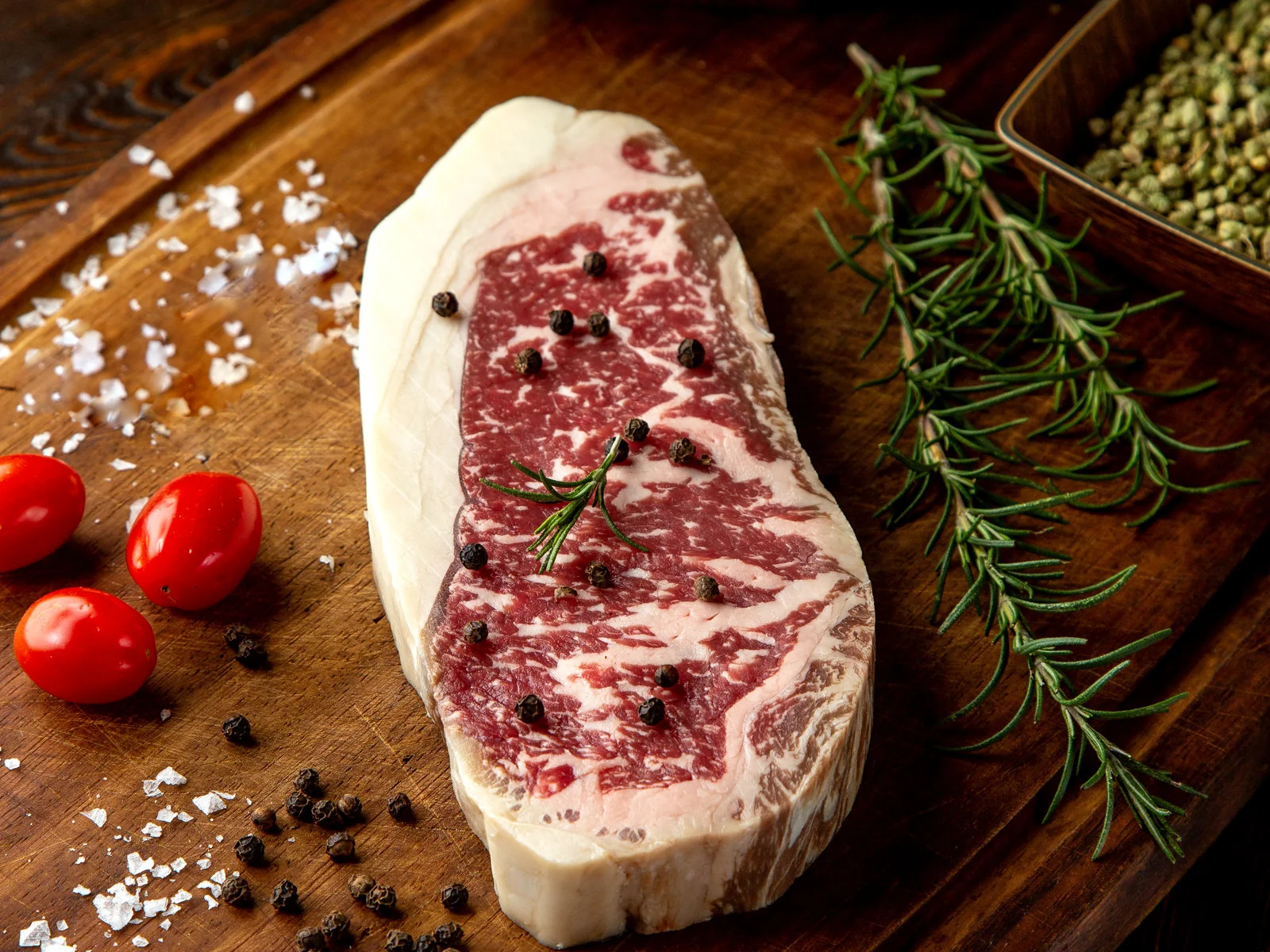 Striploin steak with rosemary and peppercorns on a board