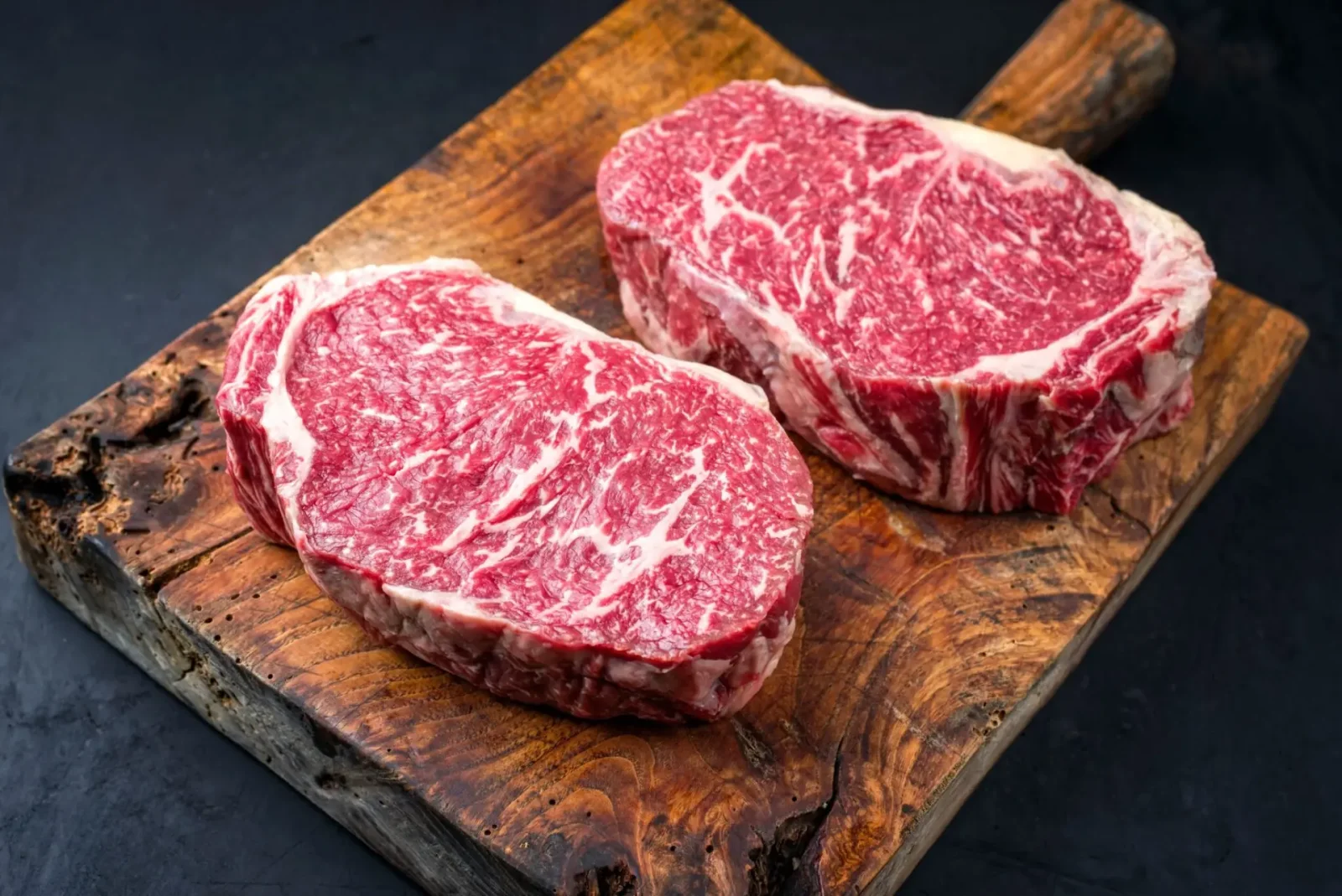 Two thick-cut Wagyu ribeye steaks showing deep marbling on a wooden board
